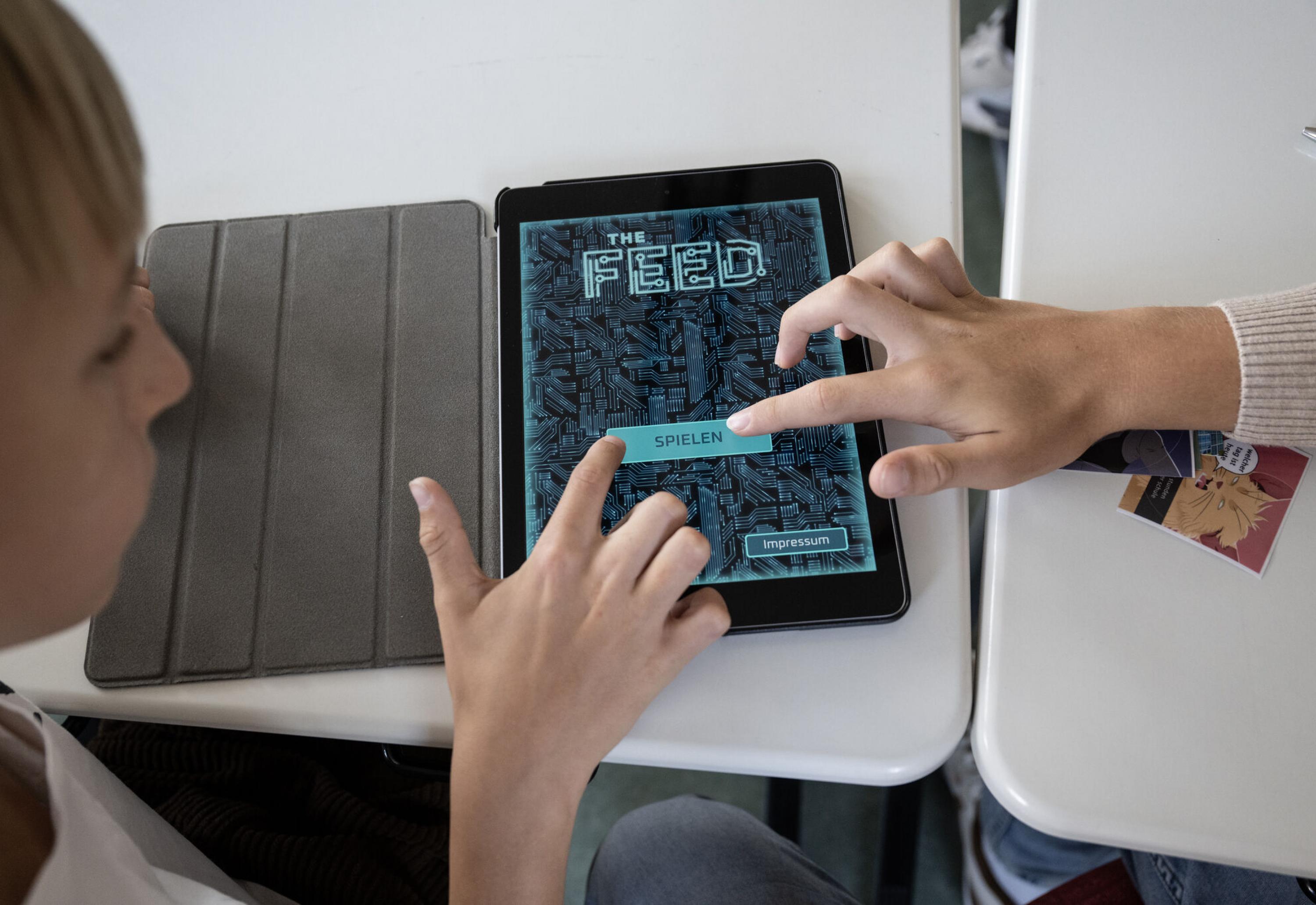 Zwei Schüler tippen gemeinsam auf den "Spielen" Button im Startmenü des Games